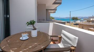 A round wooden table with a white cup and saucer, a potted plant, and a white vase on a balcony overlooking a coastal view.