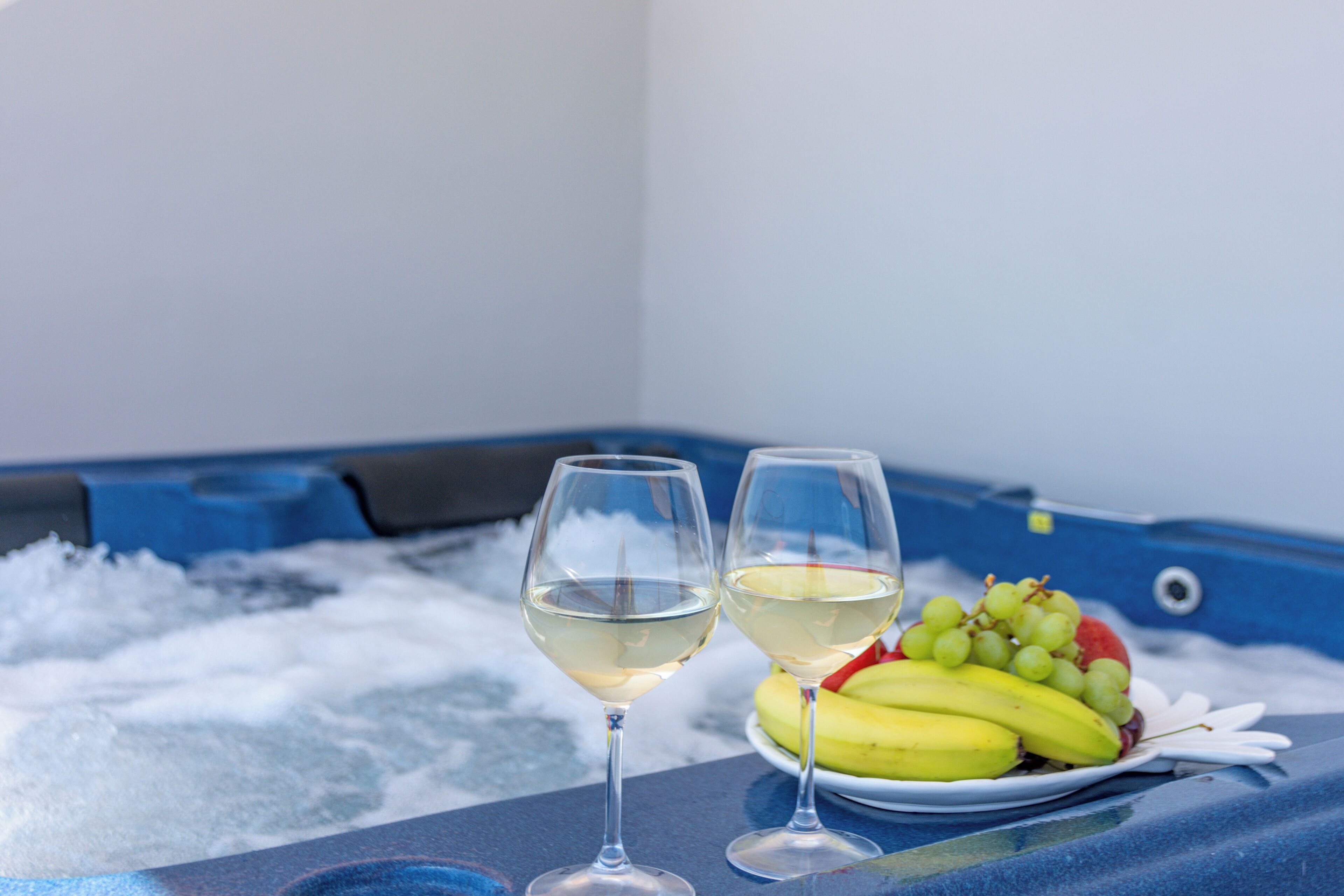 Deux verres de vin blanc et une assiette de fruits sur une table, avec une baignoire bleue en arrière-plan.