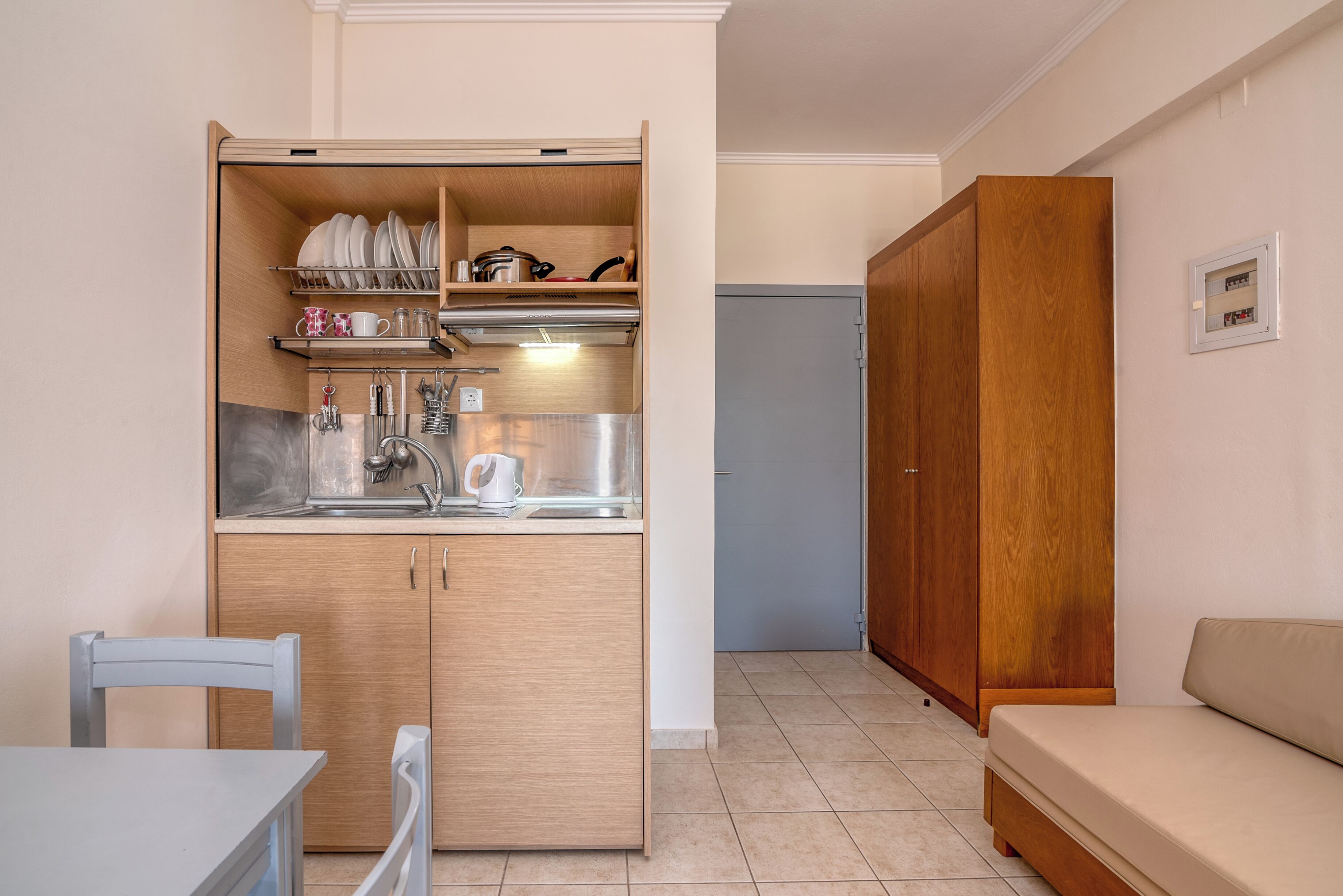 Una cocina compacta con estufa integrada, lavamanos y armarios de almacenamiento. En la zona de estar contigua hay una mesa de comedor y un sofá.