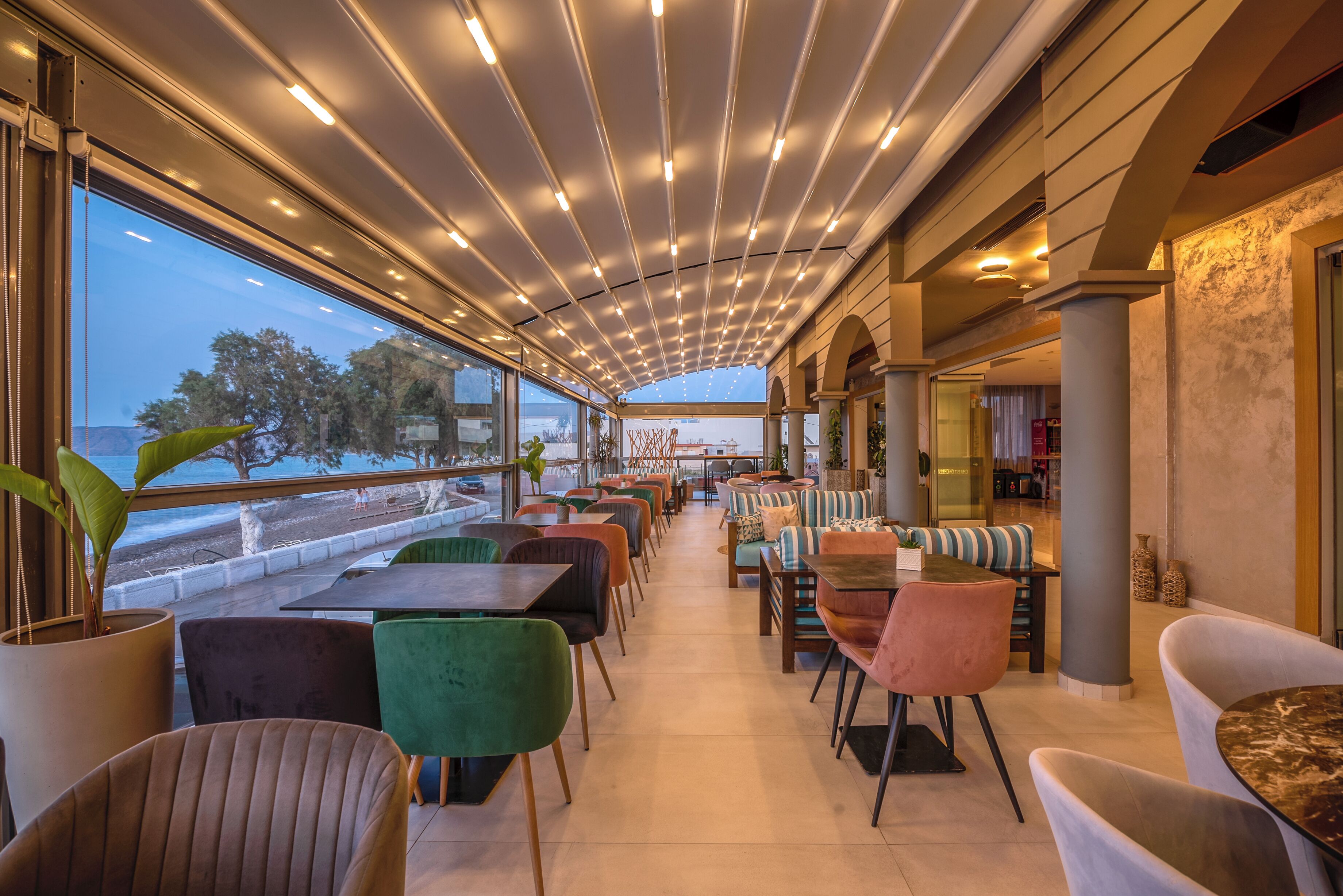 A spacious indoor seating area with a view of the sea, featuring a variety of chairs and tables.