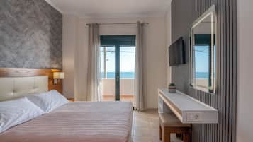 A modern hotel room with a bed, a TV, a vanity with a mirror, and a view of the sea.