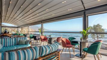 Un área de estar moderna al aire libre con vista al mar, que incluye sofás a rayas, sillas coloridas y una mesa con una planta.