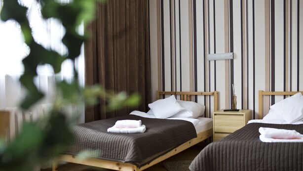 Habitación de hotel con dos camas de madera, una mesita de noche, una lámpara y vistas al exterior.