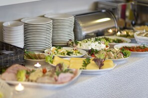 A buffet table with various dishes, plates, and a stack of bowls.