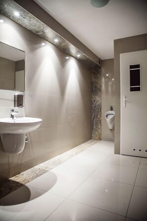 A modern bathroom with a marble accent wall, a white sink, and a urinal.