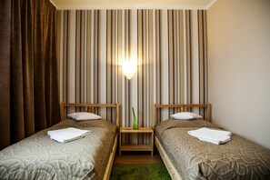 A hotel room with two single beds, a nightstand with a lamp, and a striped curtain.