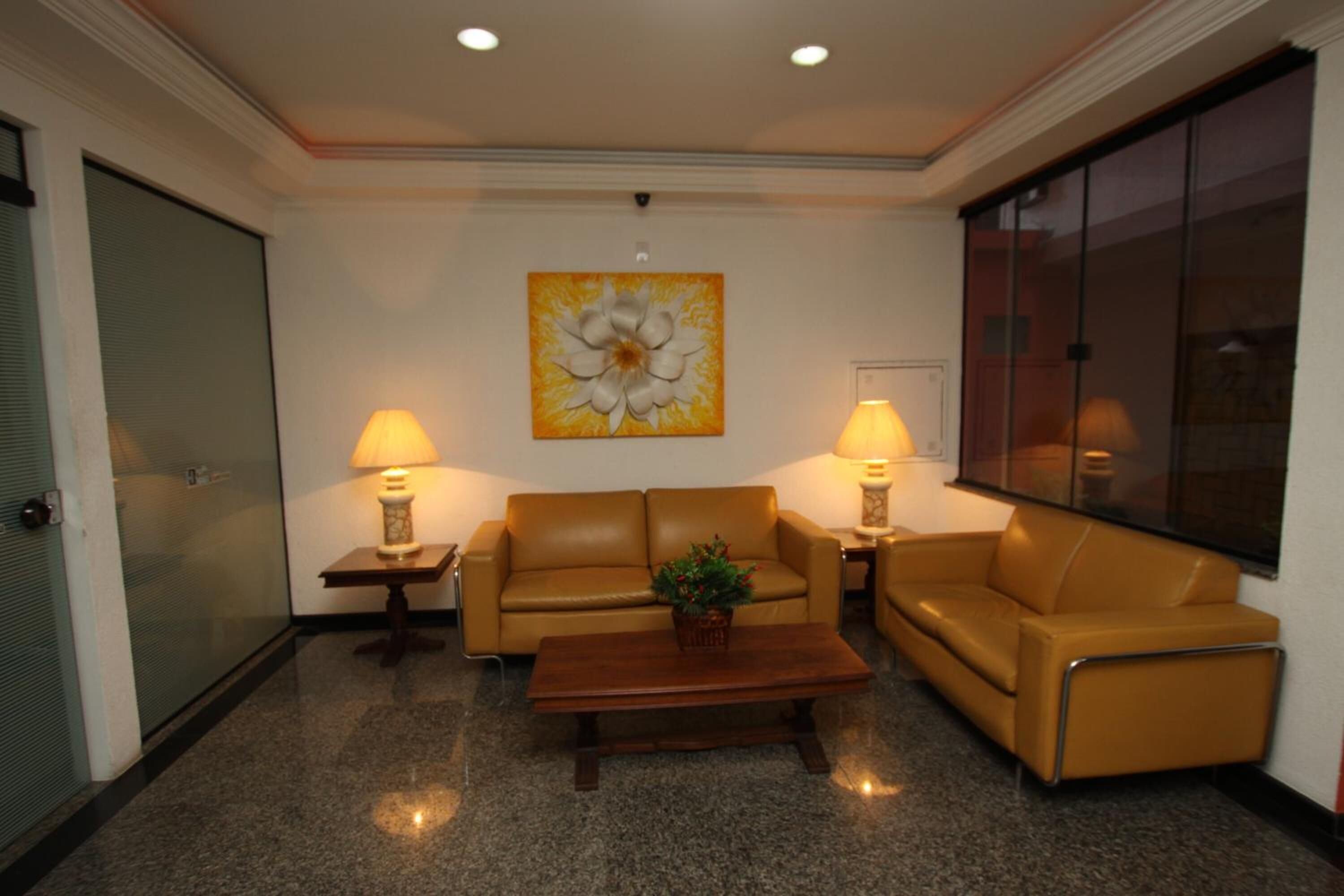 A lobby with a sofa, two lamps, a coffee table, and a large flower painting on the wall.