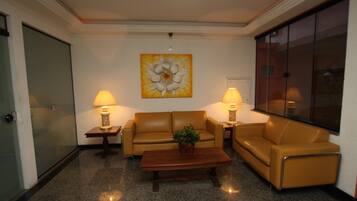 A lobby with a sofa, two lamps, a coffee table, and a large flower painting on the wall.