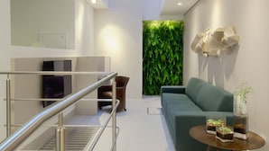 A modern living room with a green wall, a sofa, a coffee table, and a TV. - Hotel Blumenau (Balneário Camboriú)