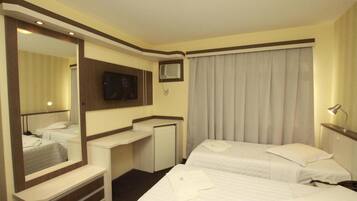 A hotel room with two beds, a desk, a mirror, a television, and a window with curtains.