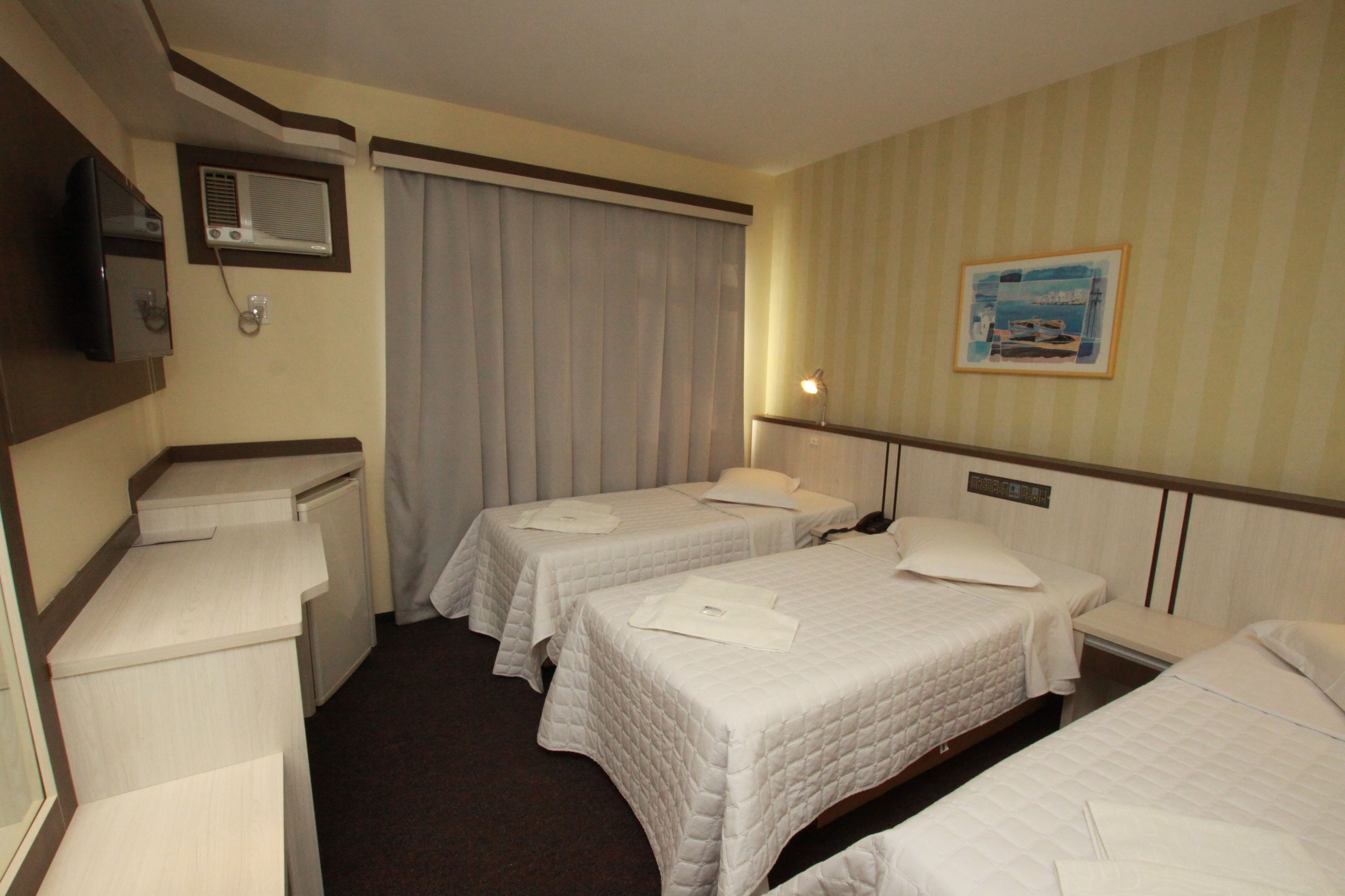 Habitación de hotel con dos camas individuales, un escritorio, una silla, un televisor y una ventana con cortinas.