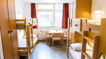 A room with bunk beds, a table, chairs, a window with curtains, and a radiator.