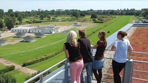 Un groupe de personnes se tient sur un point de vue surplombant un paysage verdoyant, avec des bâtiments et un sentier.