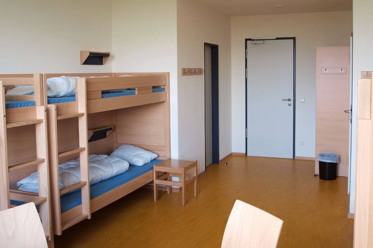 A dormitory room with bunk beds, a small table, and a door.