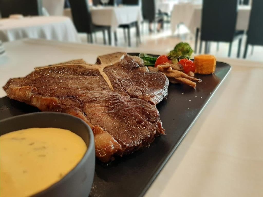 A steak with a side of vegetables and sauce on a plate.