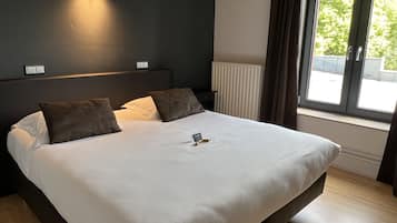 Un lit bien fait, avec une couette blanche, deux oreillers et une petite table de chevet sur laquelle se trouve une lampe.