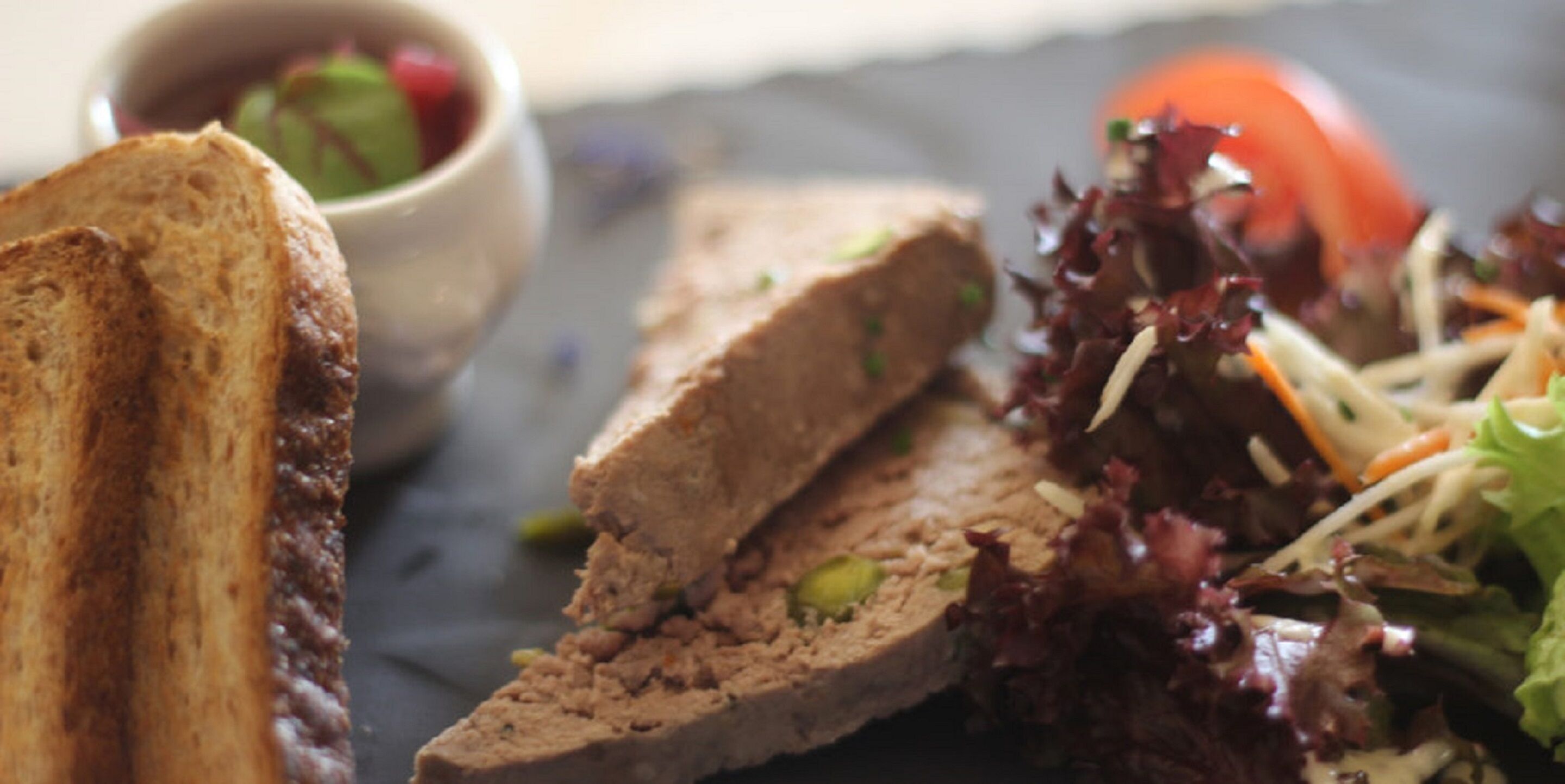 A meal consisting of a toasted bread slice, a meatloaf cut, and a salad with mixed greens and shredded carrots.