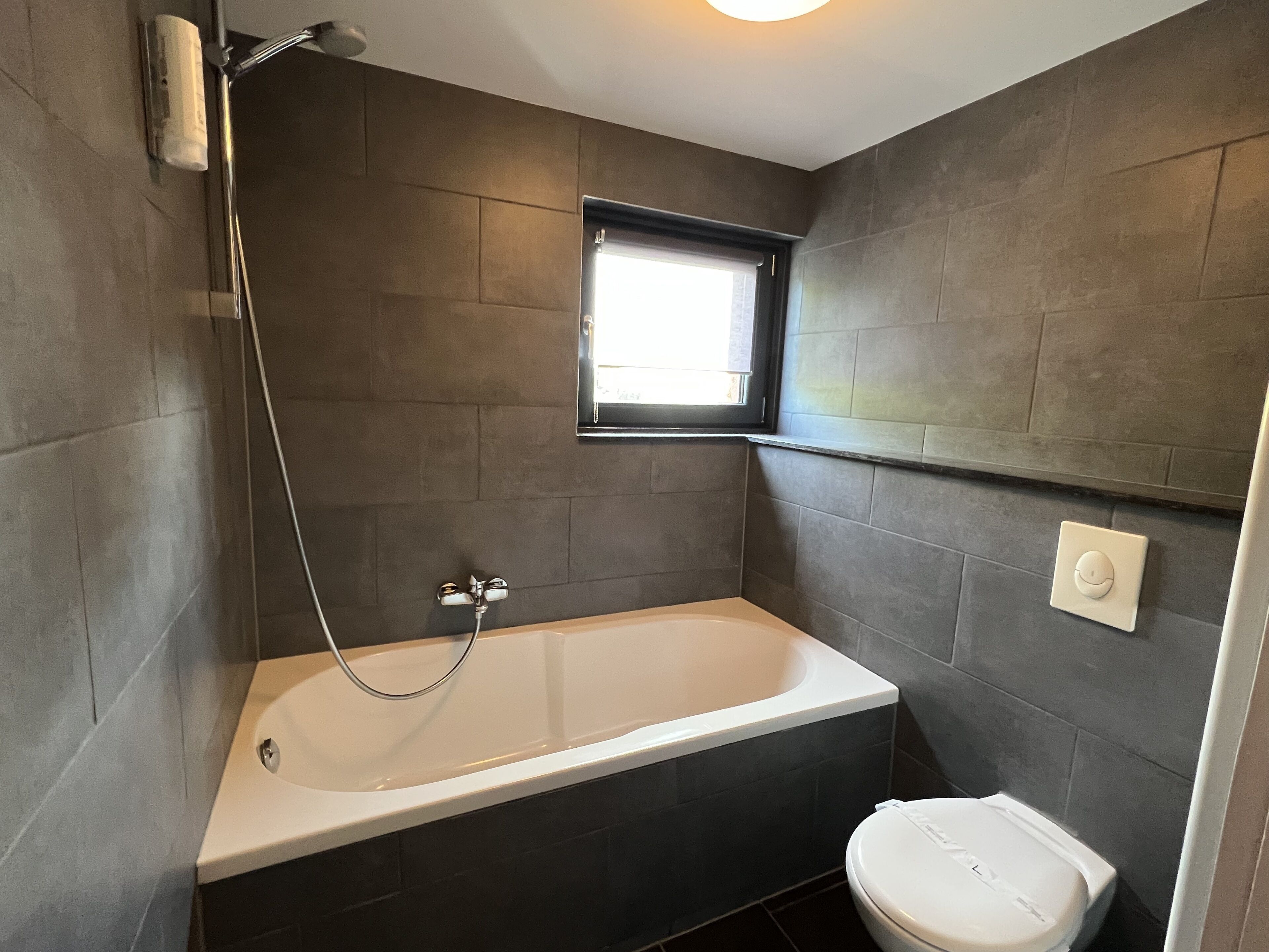 Ein modernes Badezimmer mit Badewanne, Toilette und einem Fenster für natürliches Licht.
