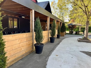 A covered outdoor seating area with wooden walls and potted plants. - Hôtel Restaurant Lamy (Troisvierges)
