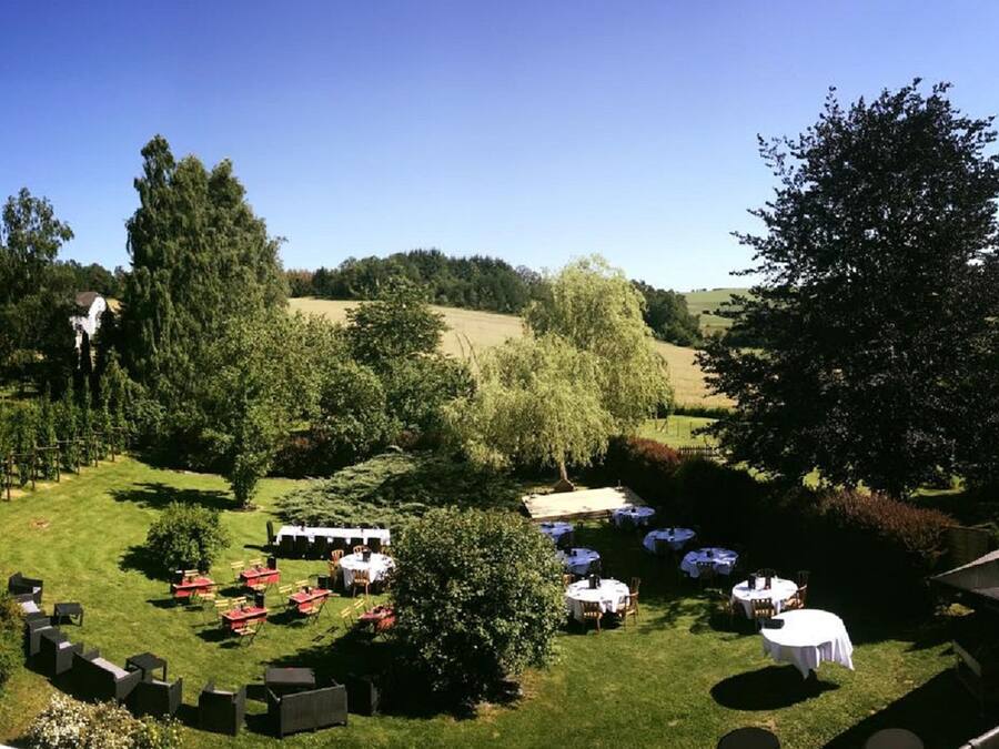An outdoor event space with tables and chairs arranged for an event, surrounded by trees and a grassy area.