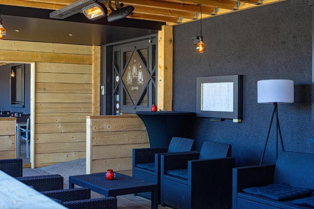 Un espace extérieur moderne, aménagé avec des meubles en osier, un téléviseur fixé au mur et une lampe.