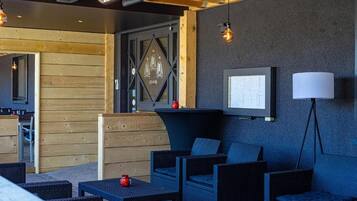 Un espace extérieur moderne, aménagé avec des meubles en osier, un téléviseur fixé au mur et une lampe.