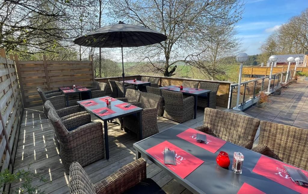 Une terrasse extérieure avec des meubles en osier, des tables avec des sets de table rouges et un grand parasol.