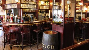 A bar area with wooden bar counters, multiple stools, and shelves stocked with glassware and bottles.