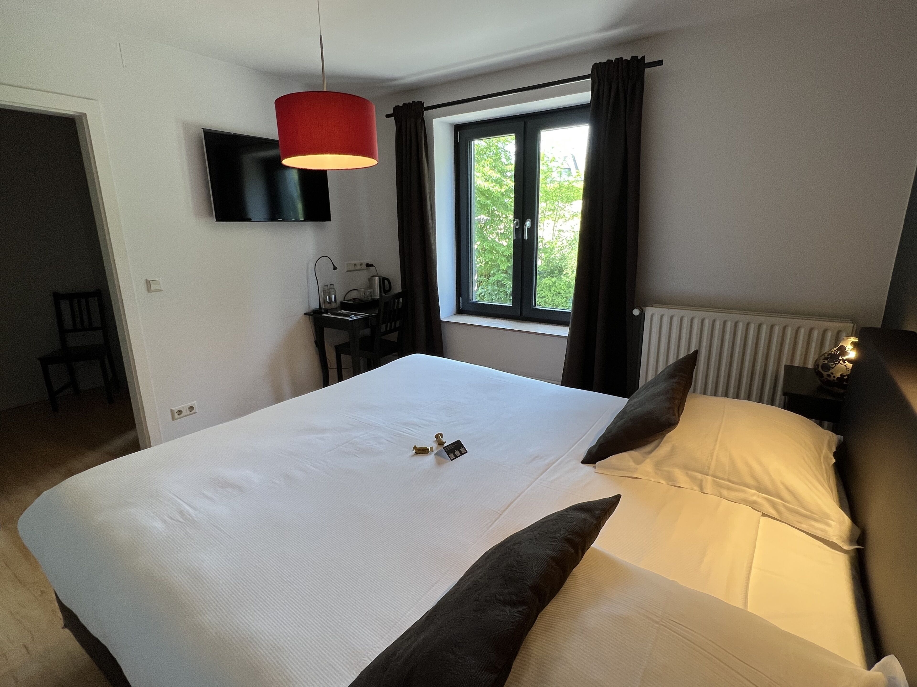 Habitación de hotel con una cama grande, un escritorio con silla, un televisor montado en la pared y una ventana con cortinas.