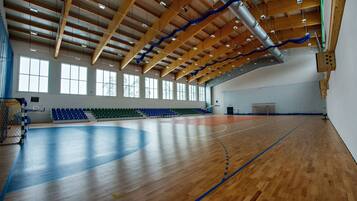 A large indoor gymnasium with a wooden floor, high ceiling with exposed beams, and multiple windows.