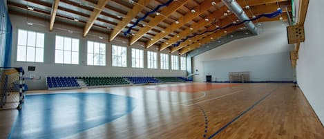 Un gimnasio amplio con piso de madera, techo alto con vigas a la vista y varias ventanas.