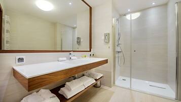 Un baño moderno con tocador de madera, un espejo grande, cabina de ducha con mampara de vidrio y toallas dobladas ordenadamente en un estante.