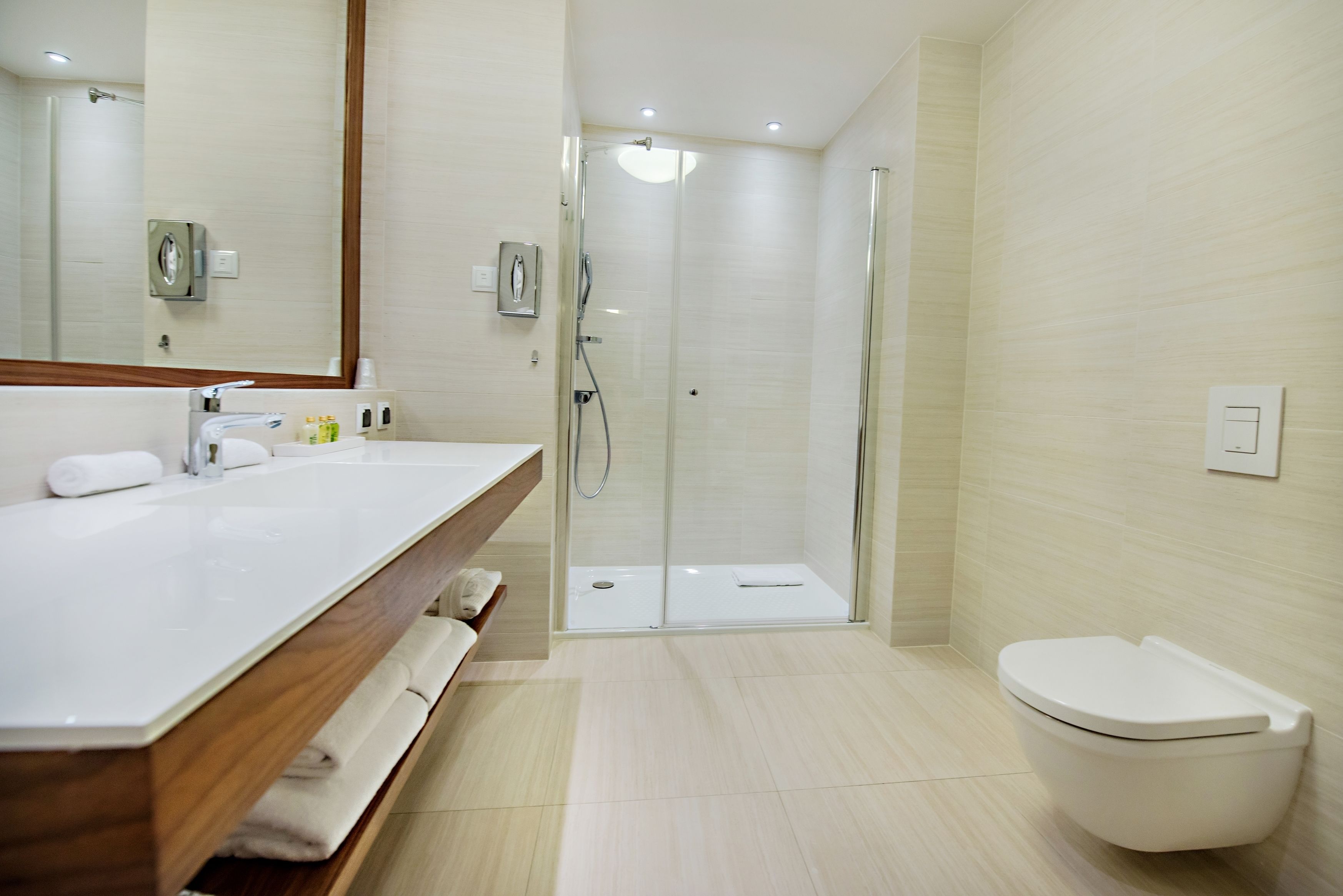 Un baño moderno con tocador de madera, cabina de ducha de vidrio y un inodoro blanco.