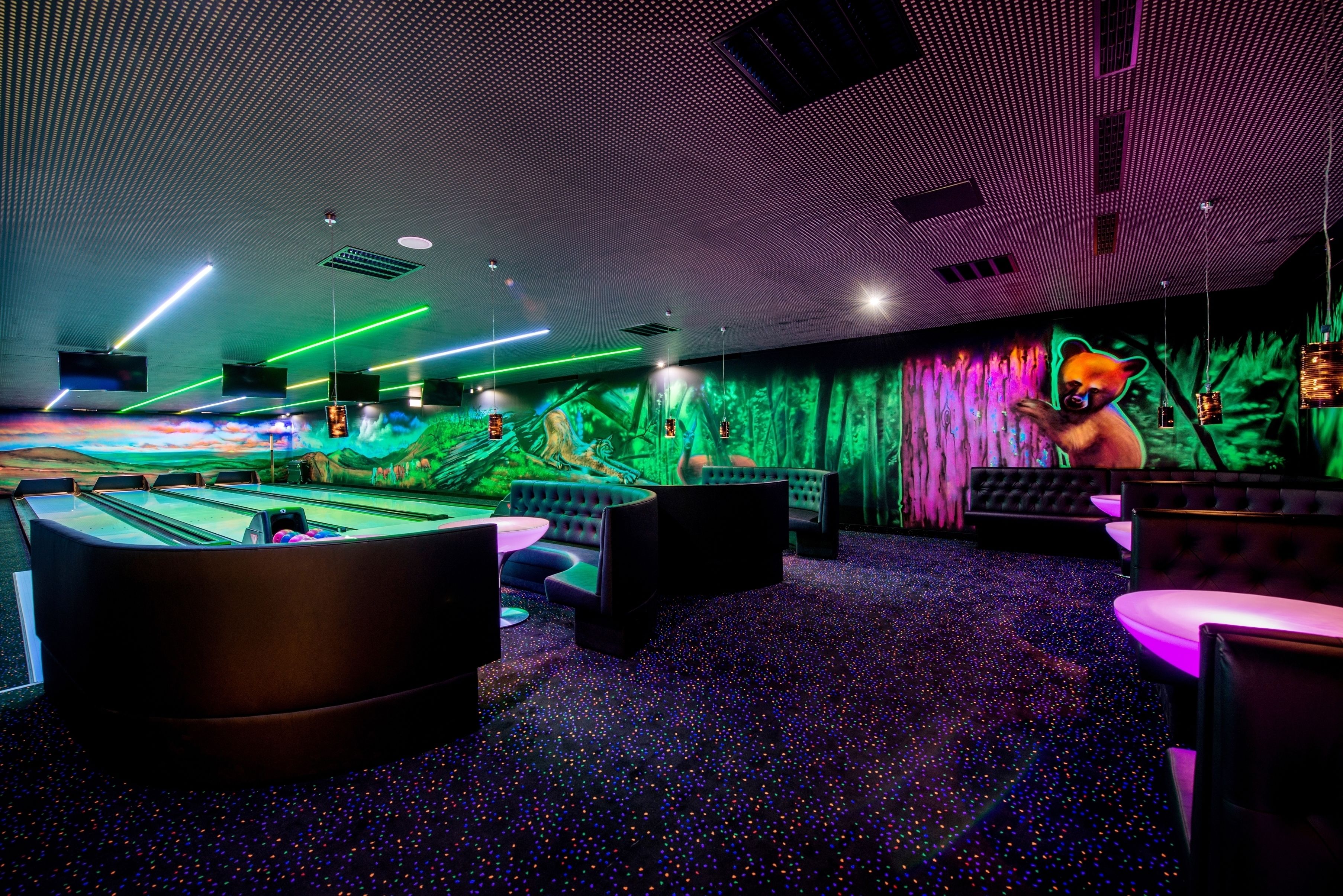 Una sala de billar con mesa de pool, zonas de estar y una pared iluminada y colorida.