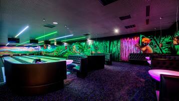 Una sala de billar con mesa de pool, zonas de estar y una pared iluminada y colorida.
