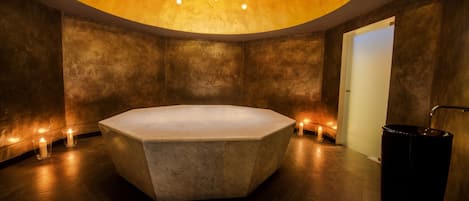 A modern bathroom with a large, oval-shaped bathtub, recessed ceiling lights, and a black trash can.
