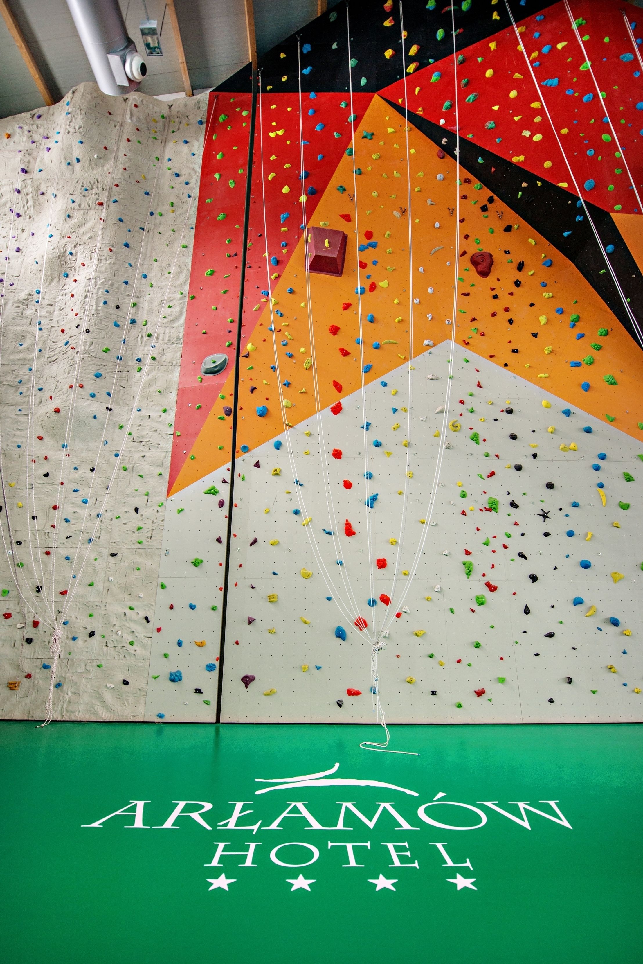 Un mur d’escalade avec des prises de différentes couleurs et une banderole verte sur laquelle on peut lire « AREAMOW HOTEL ».