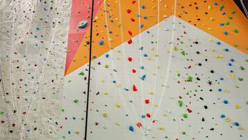 Un mur d’escalade avec des prises de différentes couleurs et une banderole verte sur laquelle on peut lire « AREAMOW HOTEL ».