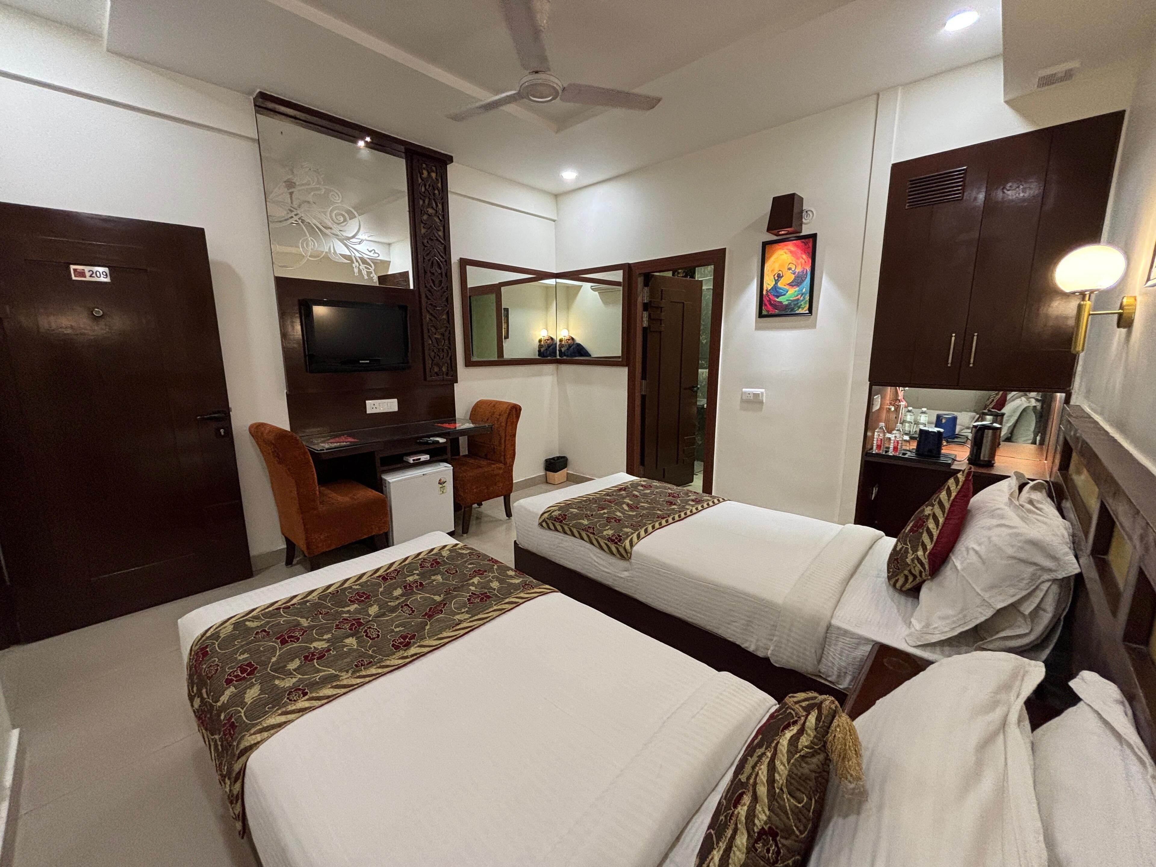 A hotel room with two single beds, a desk with a chair, a television, a mirror, and a wardrobe.