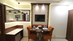 A hotel room with a dining table, two chairs, a TV mounted on the wall, a coffee maker, and a small cabinet. - Hotel Taj Inn (Agra)