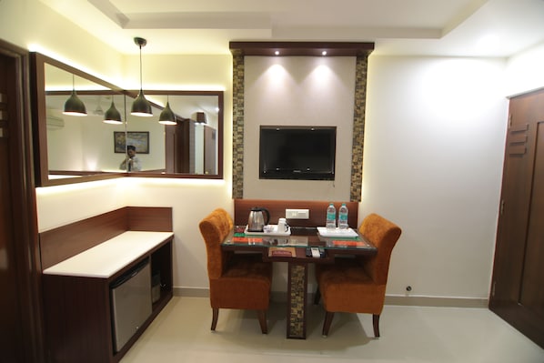 Habitación de hotel con una mesa de comedor, dos sillas, un televisor montado en la pared, una cafetera y un mueble pequeño.