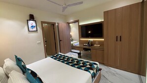 A modern hotel room with a large bed, a desk with a flat-screen TV, a ceiling fan, and wooden wardrobes. - Hotel Taj Inn (Agra)