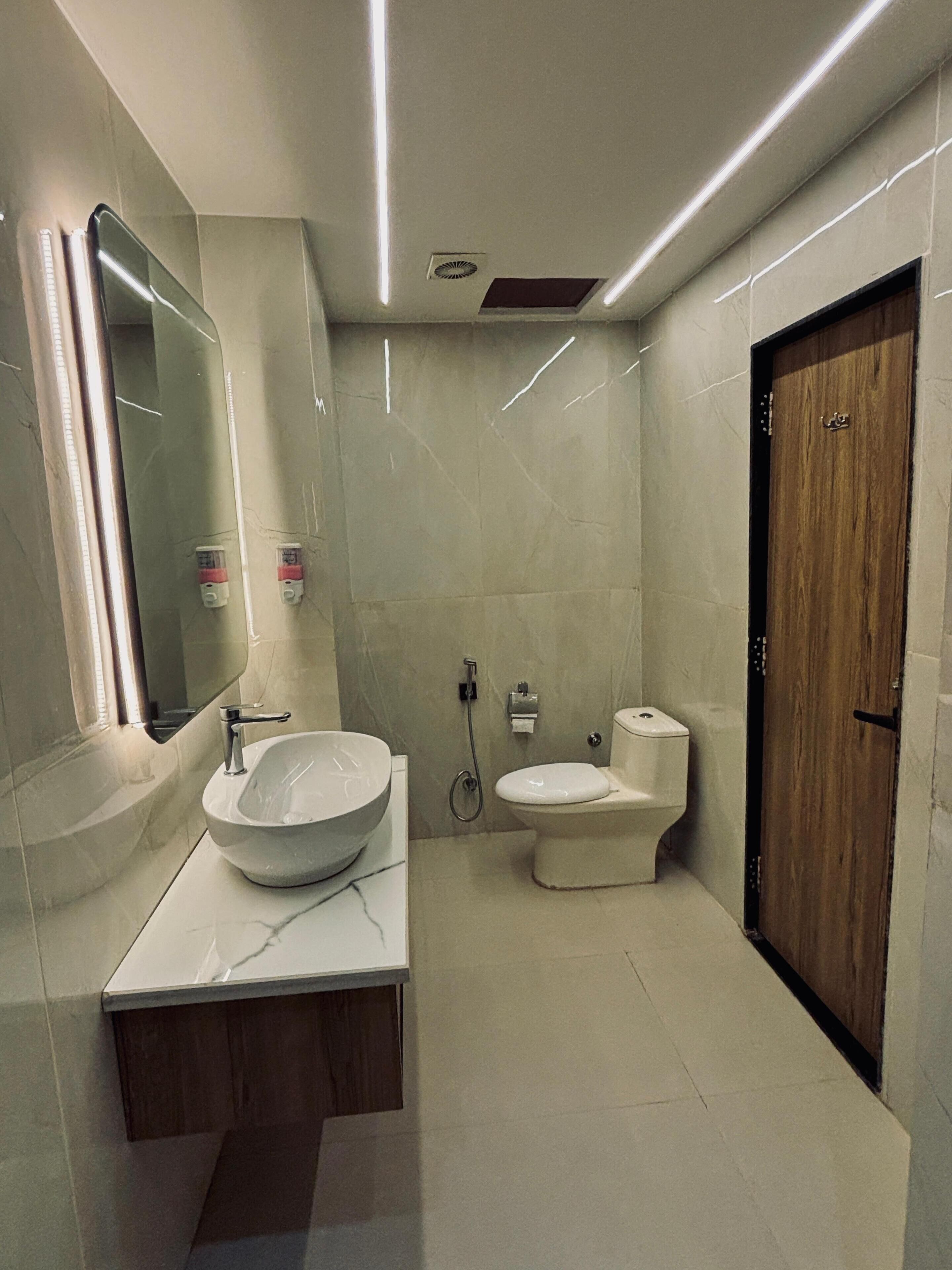 Ein modernes Badezimmer mit einem großzügigen Aufsatzbecken, einer Toilette und einer Holztür.