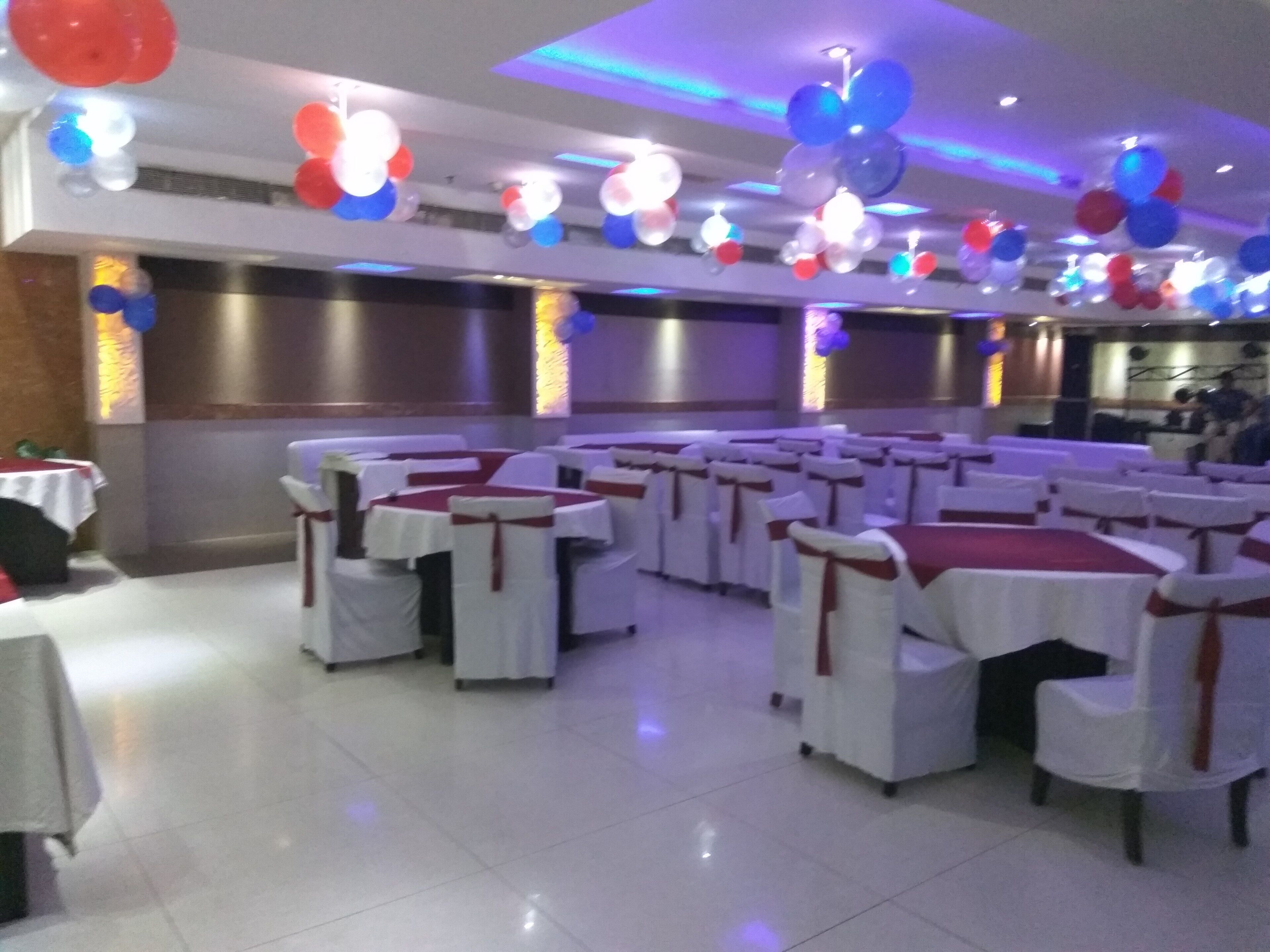 Salão de festas com mesas e cadeiras redondas, decorado com balões.