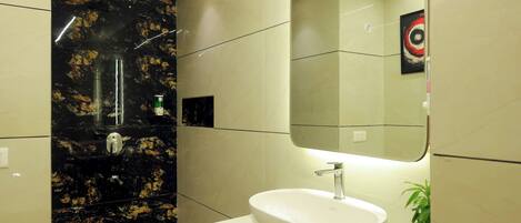 A modern bathroom with a white sink, a large mirror, and a black marble shower wall.