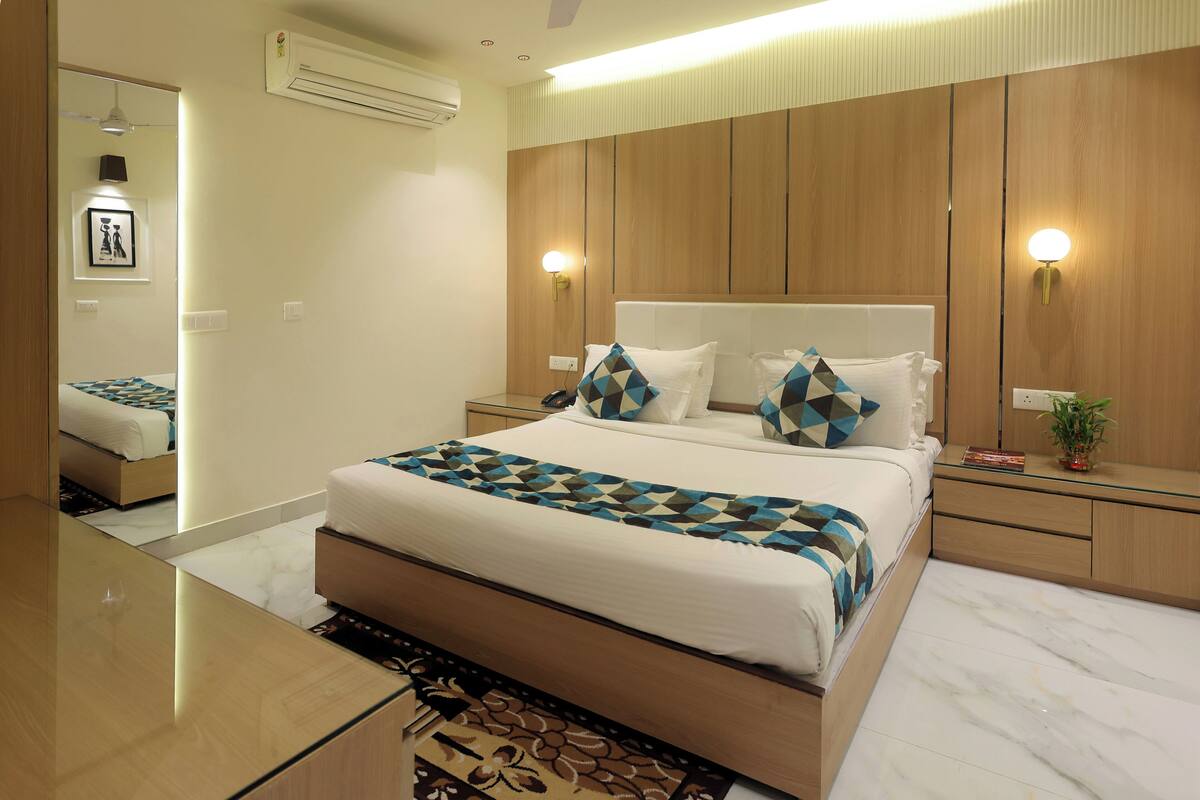 A modern bedroom with a large bed, wooden headboard, bedside tables, and a mirror.