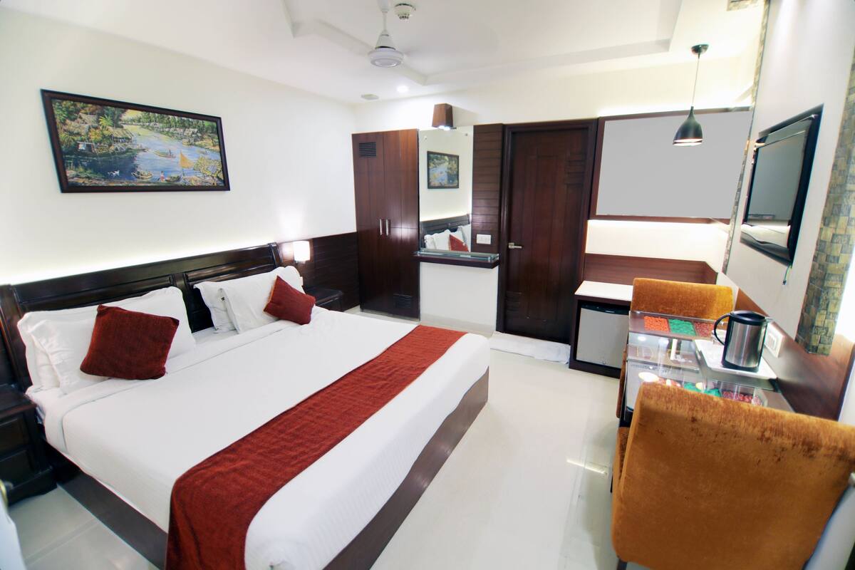 A hotel room with a large bed, a desk with a chair, a TV, and a painting on the wall.