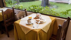 A table set for breakfast with a yellow tablecloth, a cup of coffee, a plate of pancakes, and a glass of orange juice.