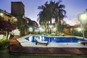 Ein Pool mit Liegestühlen, umgeben von Palmen und einer Holzterrasse.