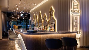 A bar area with a curved counter, bar stools, and a decorative wall with illuminated designs. - Motel One Rostock (Rostock)
